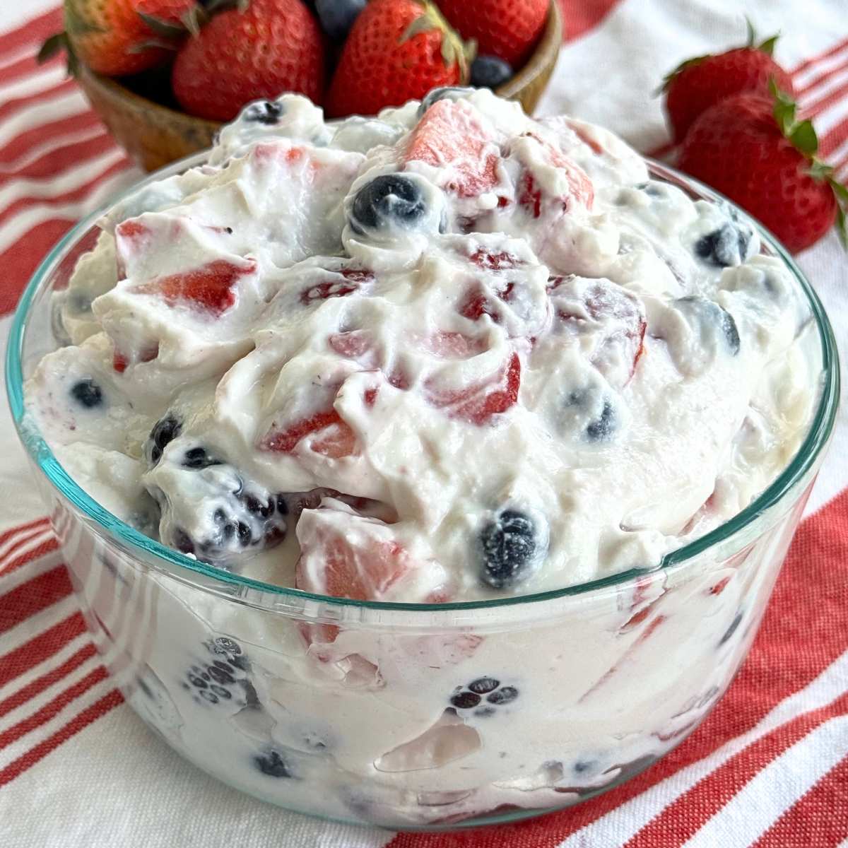 Whipped cottage cheese fruit salad with strawberries, blueberries, and blackberries in a glass bowl with strawberries behind it.