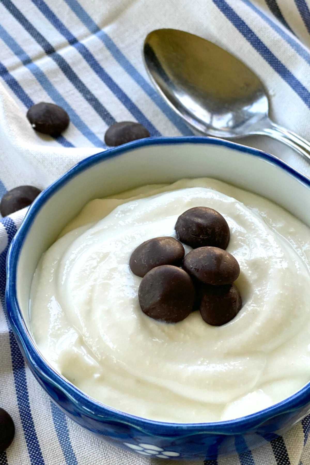 Whipped cottage cheese pudding in a blue bowl with several chocolate chips on top and a spoon behind the bowl.