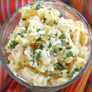 Mexican street corn in a glass cup topped with Cotija cheese and chopped cilantro on a colorful napkin.