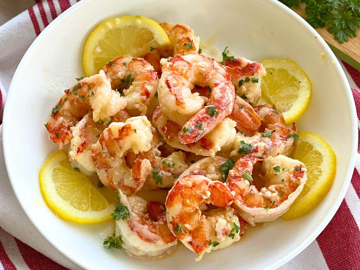 About 15 Argentine shrimp scampi surrounded by lemon slices in a white bowl.