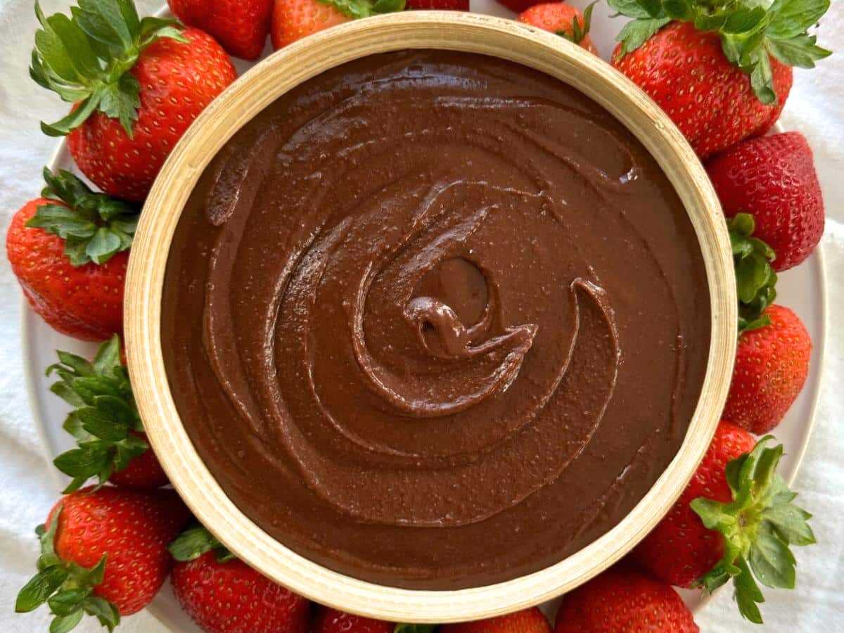 Brownie batter hummus in a cream bowl surrounded by whole strawberries.