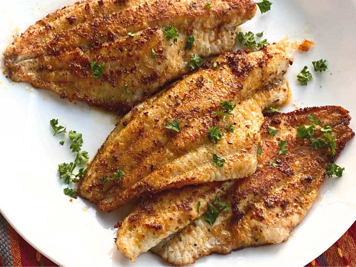 Four Cajun catfish filets sprinkled with parsley on a white plate.