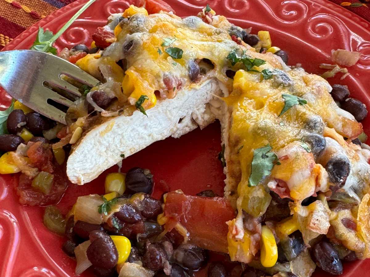 Cowboy chicken topped with black beans, tomatoes, and cheese, cut in half on a red plate.