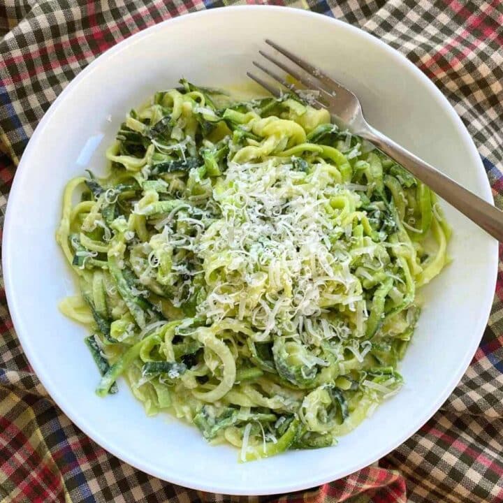 Zucchini noodle Alfredo topped with Parmesan cheese in a white bowl with a fork.