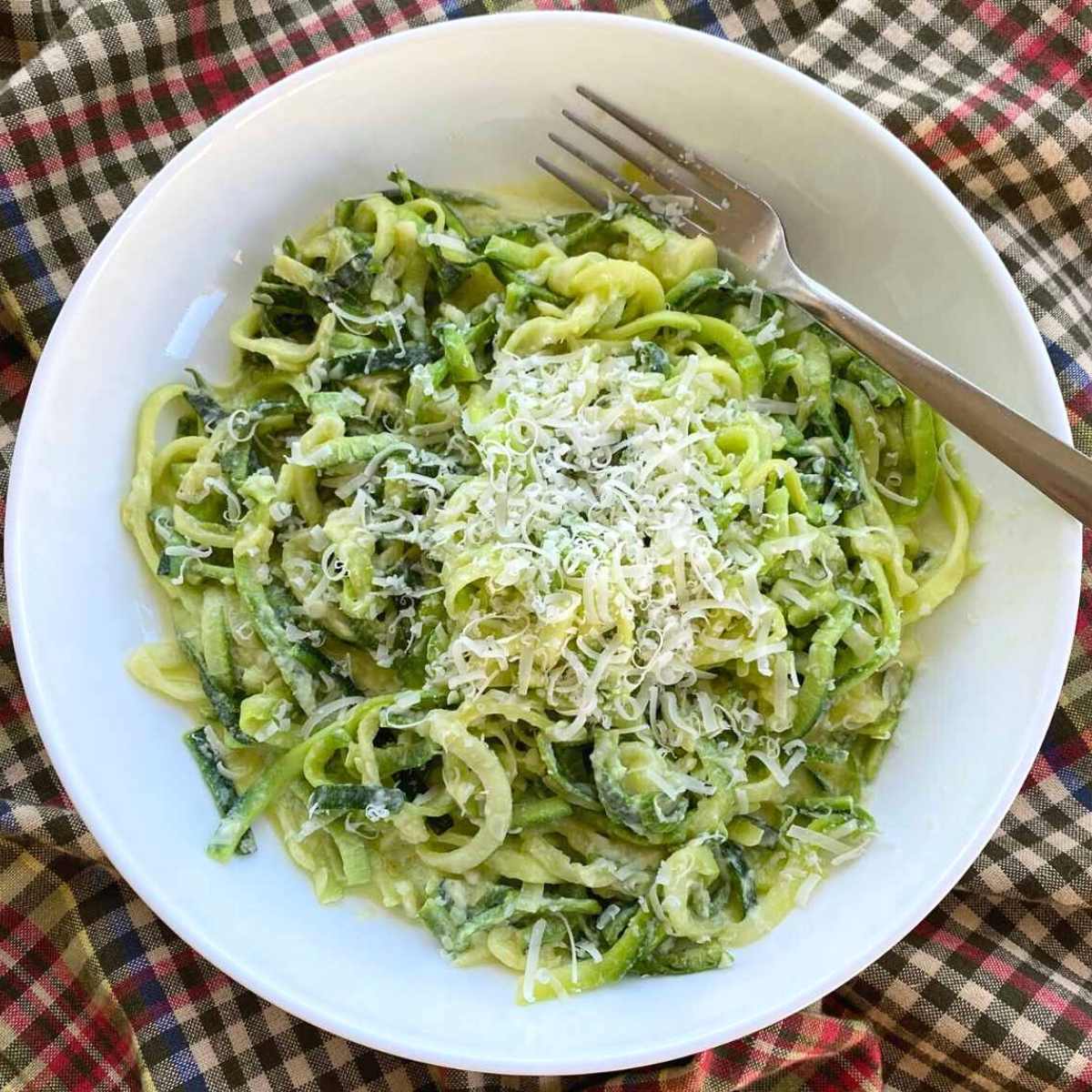 Zucchini noodle Alfredo topped with Parmesan cheese in a white bowl with a fork.