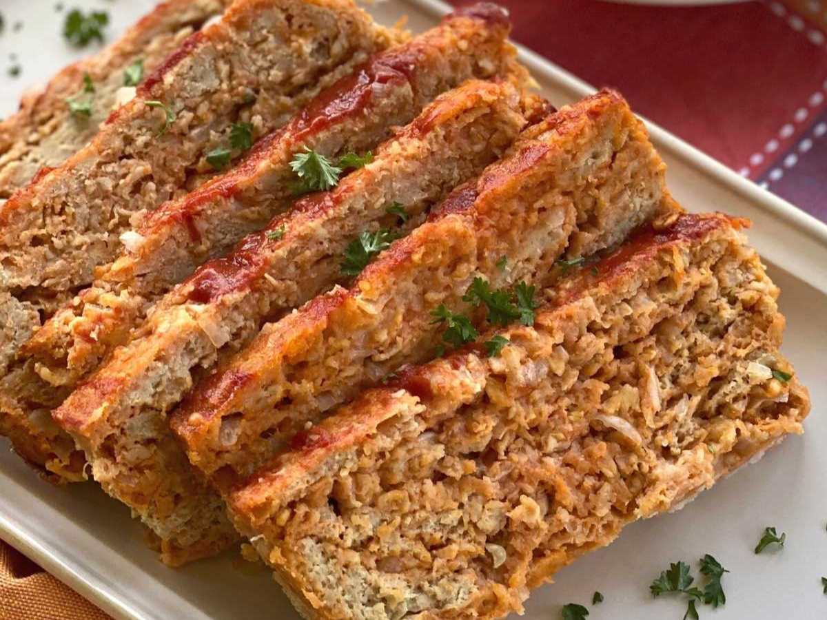 Six slices of ground chicken meatloaf on a white platter with a few pieces of chopped parsley on top.