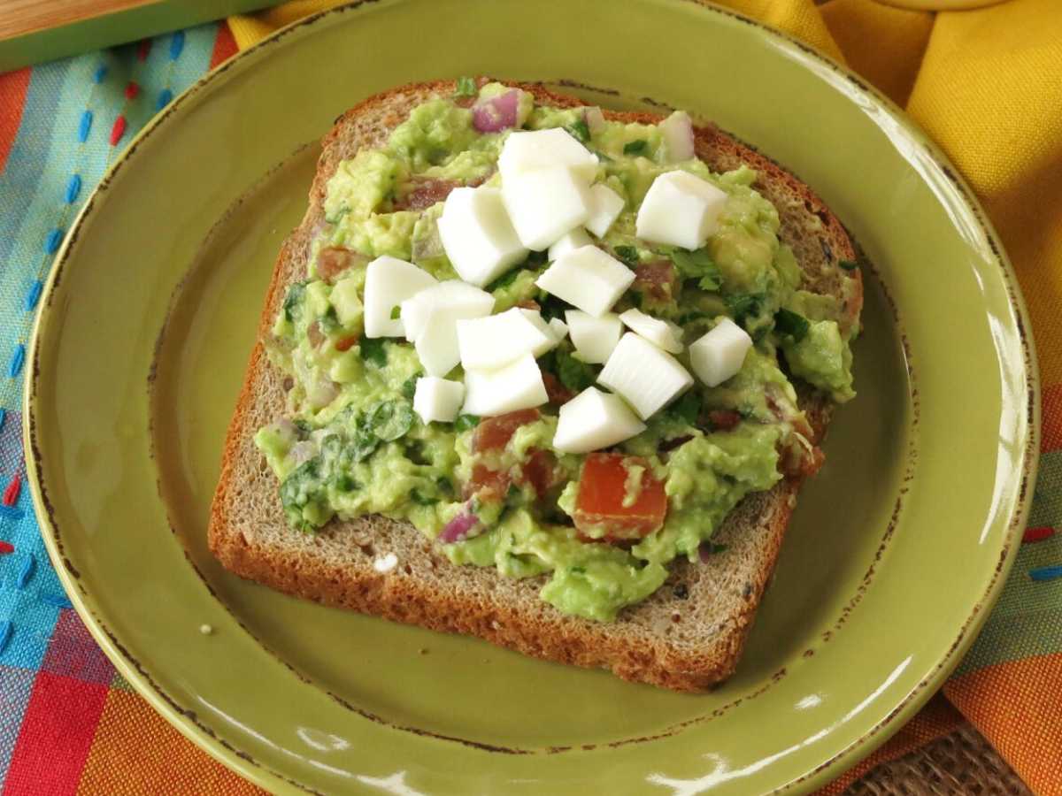 Slice of guacamole toast topped with chopped egg on a green plate.
