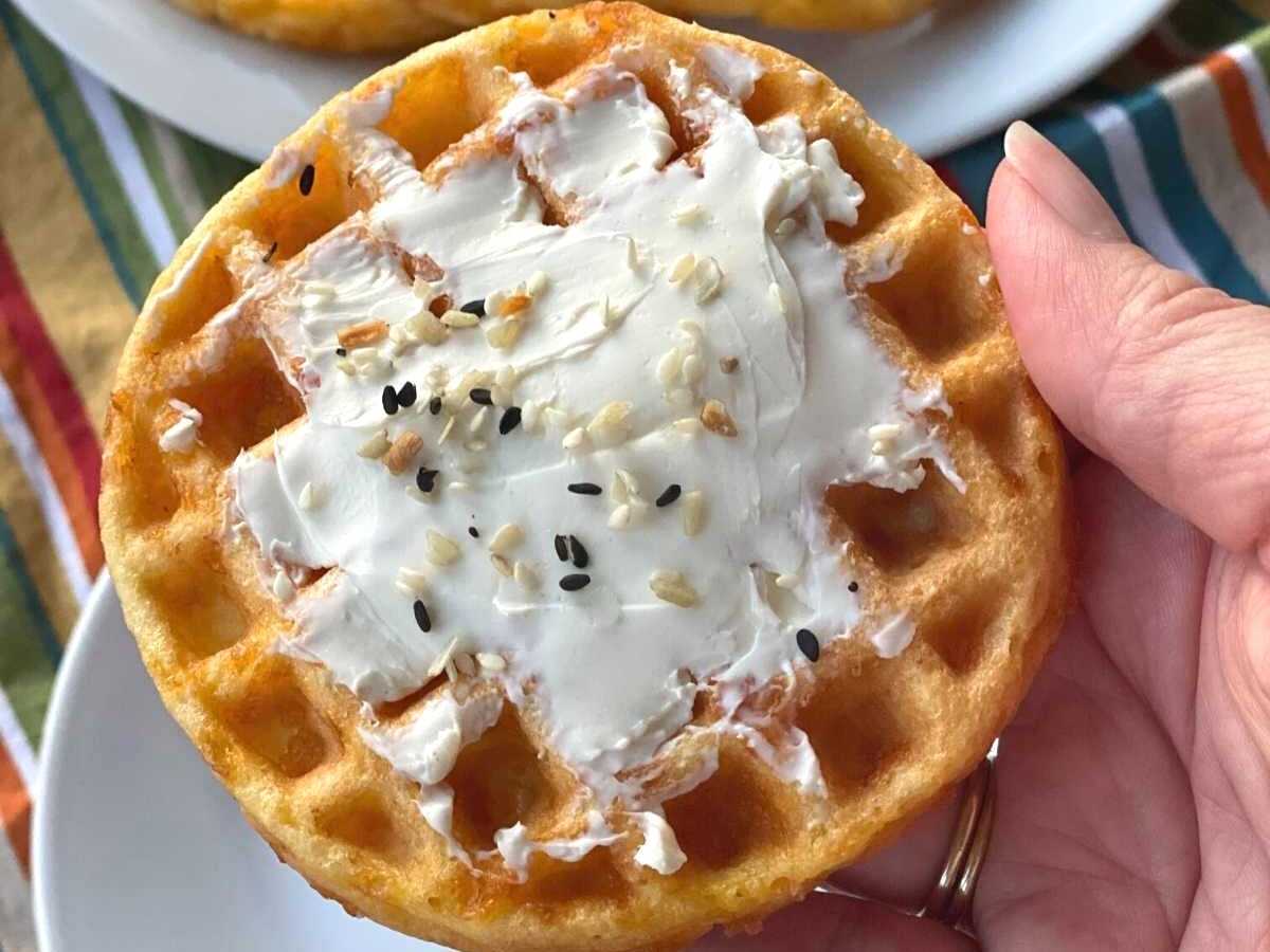 Hand holding a keto chaffle that has cream cheese spread on top.