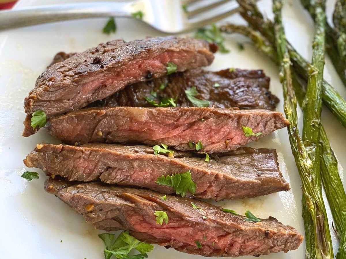 Four slices of stovetop bavette steak next to roasted asparagus on a white plate. 