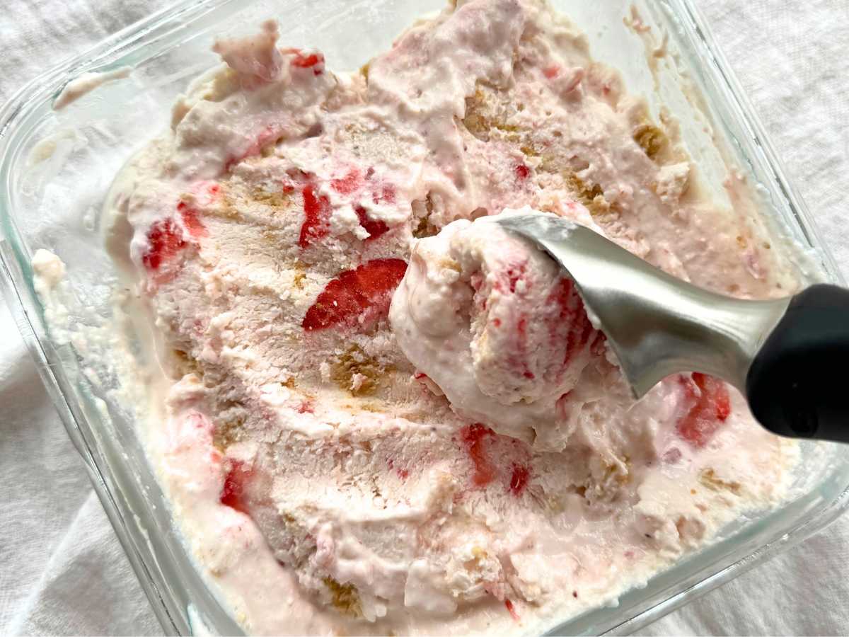 Scoop removing strawberry cottage cheese ice cream from shallow glass container.