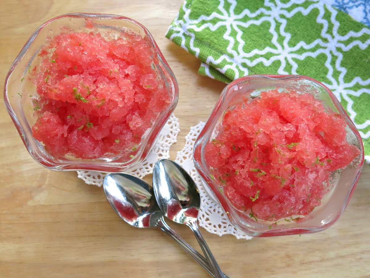 Two glass dishes with watermelon granita with two spoons and a breen patterned napkin.