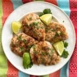 White plate with four baked chili lime chicken using tajin seasoning with lime wedges and cilantro.