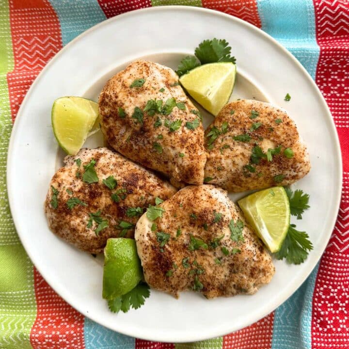White plate with four baked chili lime chicken using tajin seasoning with lime wedges and cilantro.