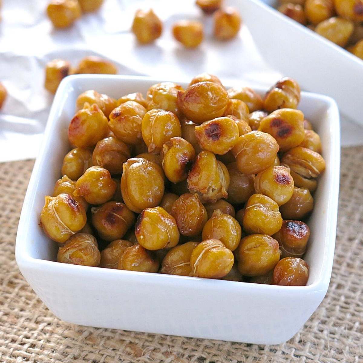 Roasted buffalo chickpeas in a square white bowl with more on parchment paper behind it.