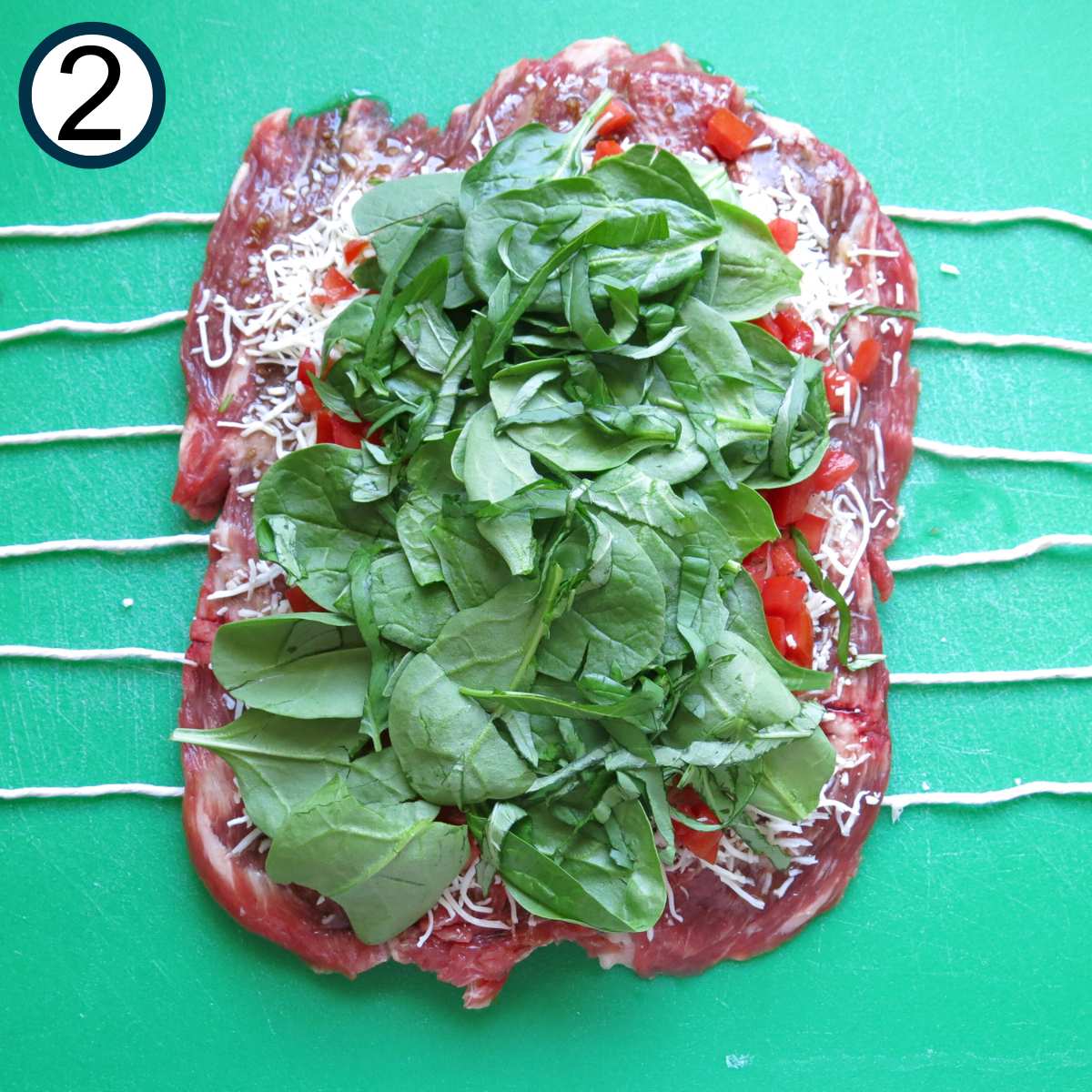 Shredded mozzarella cheese, diced tomatoes, and spinach leaves on top of a butterflied flank steak.
