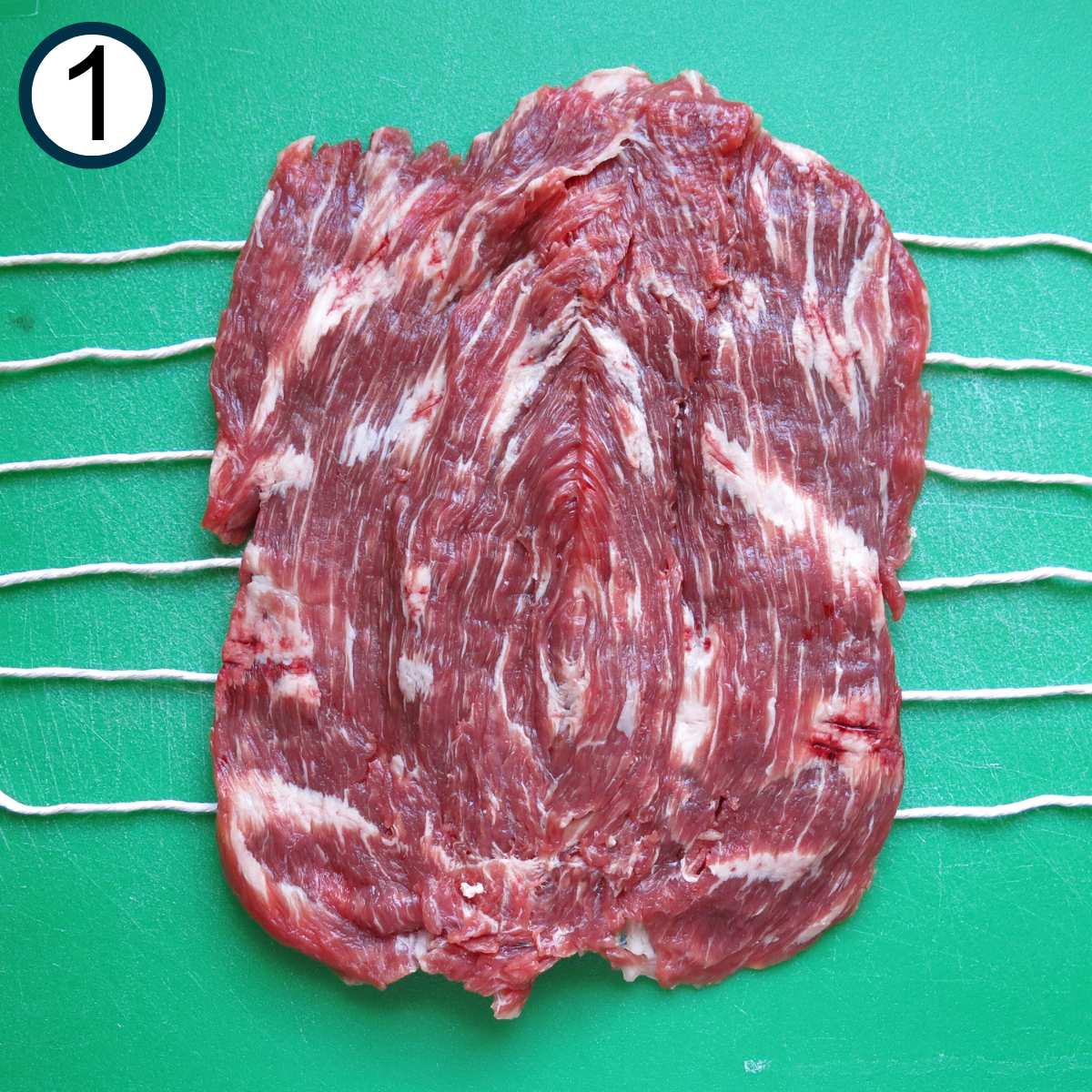 Butterflied flank steak on top of twine that's extended about 2 inches from the end of the meat.