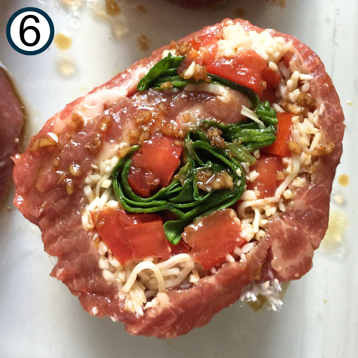 Close up of a cooked flank steak pinwheel stuffed with spinach, cheese, and tomatoes.