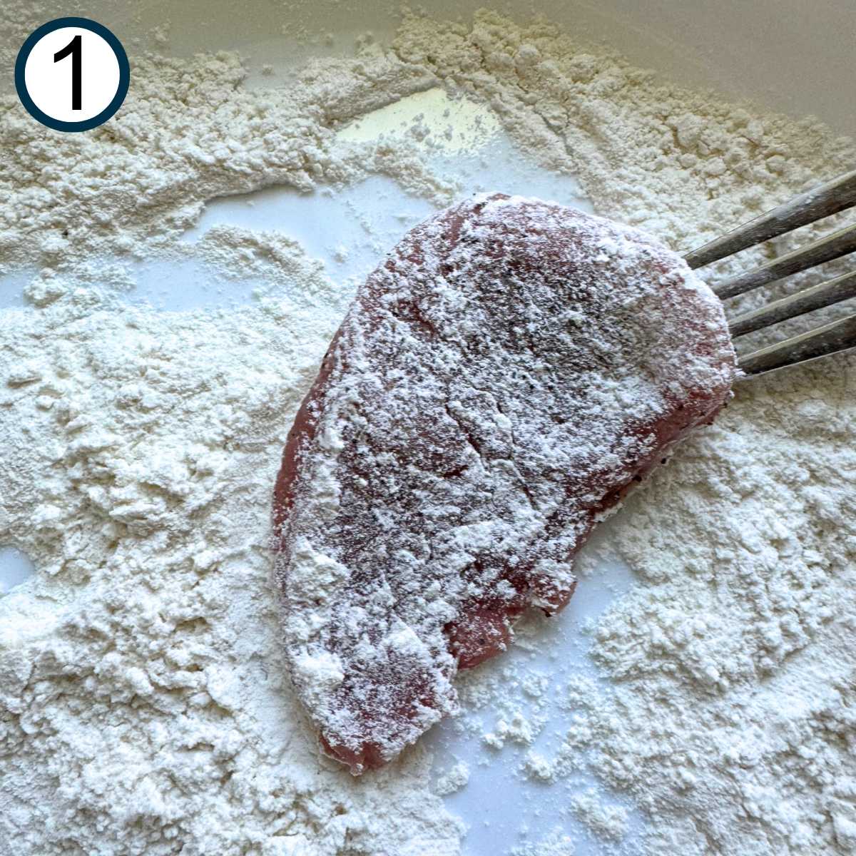 Tork holding a pork medallion lightly dusted in flour over a shallow bowl with flour.