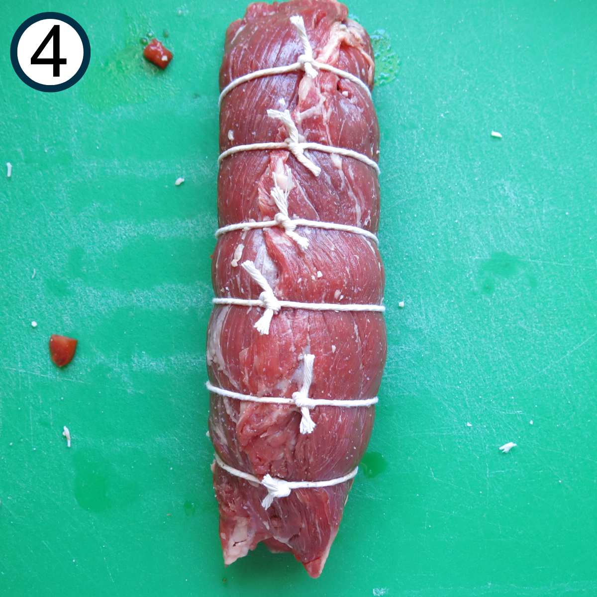 Rolled flank steak with pieces of twine tied at one inch intervals.