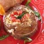Flank steak pinwheel stuffed with spinach, tomatoes, and mozzarella cheese on a red plate.