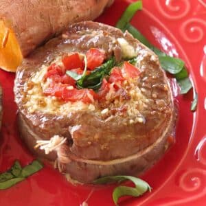 Flank steak pinwheel stuffed with spinach, tomatoes, and mozzarella cheese on a red plate.