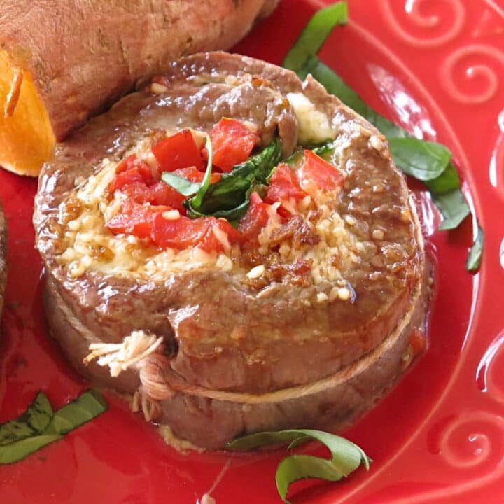 Flank steak pinwheel stuffed with spinach, tomatoes, and mozzarella cheese on a red plate.