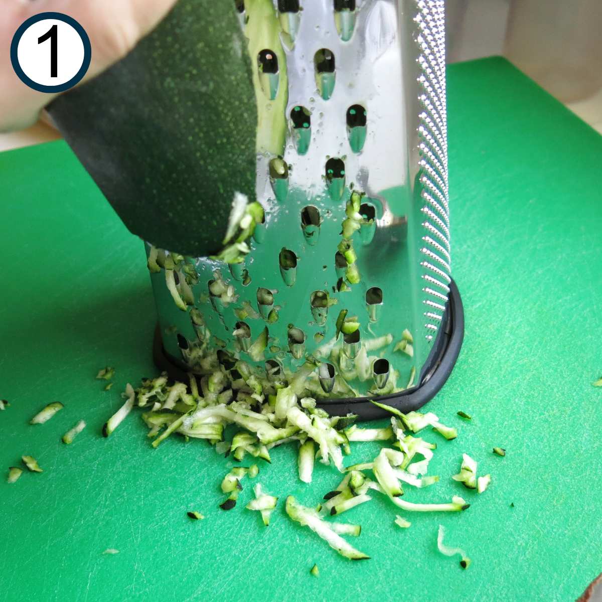 Zucchini being grated with the large holes of a box grater.
