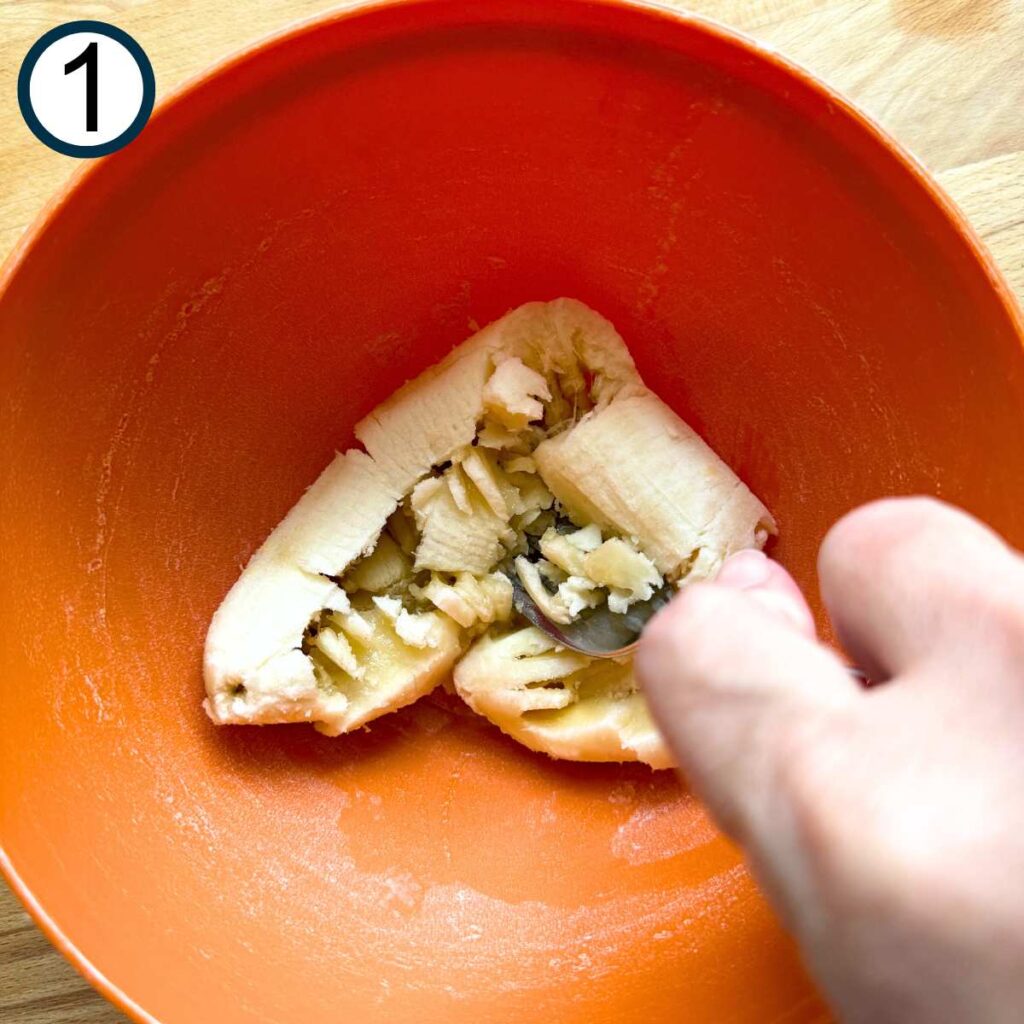 Bananas being mashed with a fork in an orange bowl.