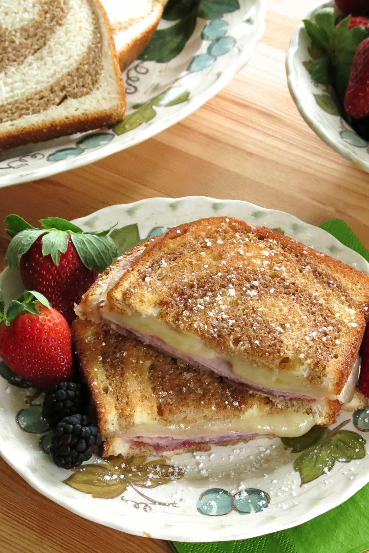 Monte cristo grilled cheese sprinkled with powedered sugar on a plate with strawberries and blackberries.
