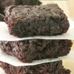 Stack of three fudgy zucchini brownies separated by parchment paper on a butcher block table top with text overlay that says "Mouthwatering Zucchini Brownies."