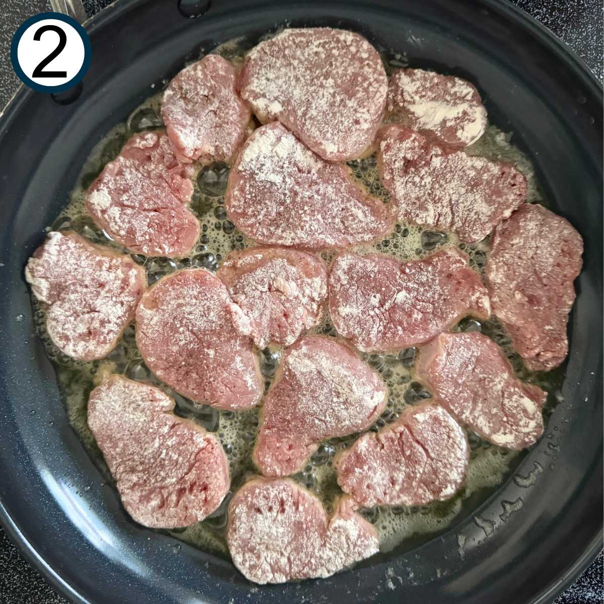 Pork medallions in a black skillet with butter and olive oil.