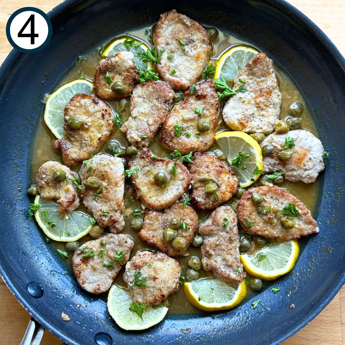 Skillet with cooked chicken piccata with lemon slices tucked around the edges and fresh parsley sprinkled over the top.