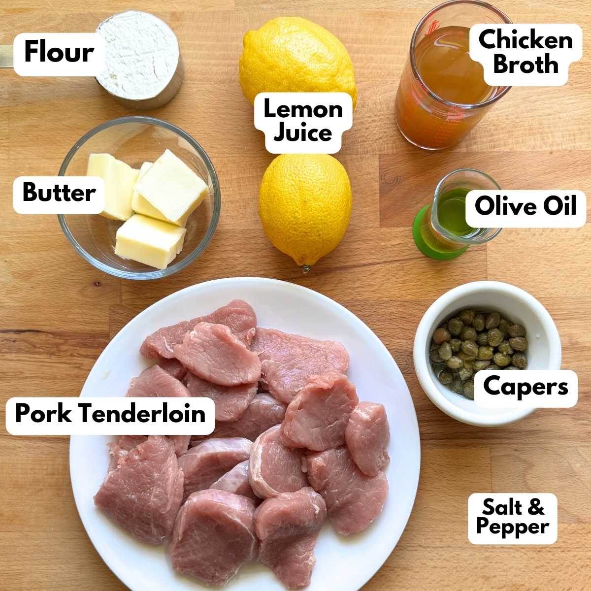Labeled ingredients to make pork tenderloin piccata: flour, 2 lemons, chicken broth, 4 cubes of butter, olive oil, capers, pork tenderloin cut into medallions.