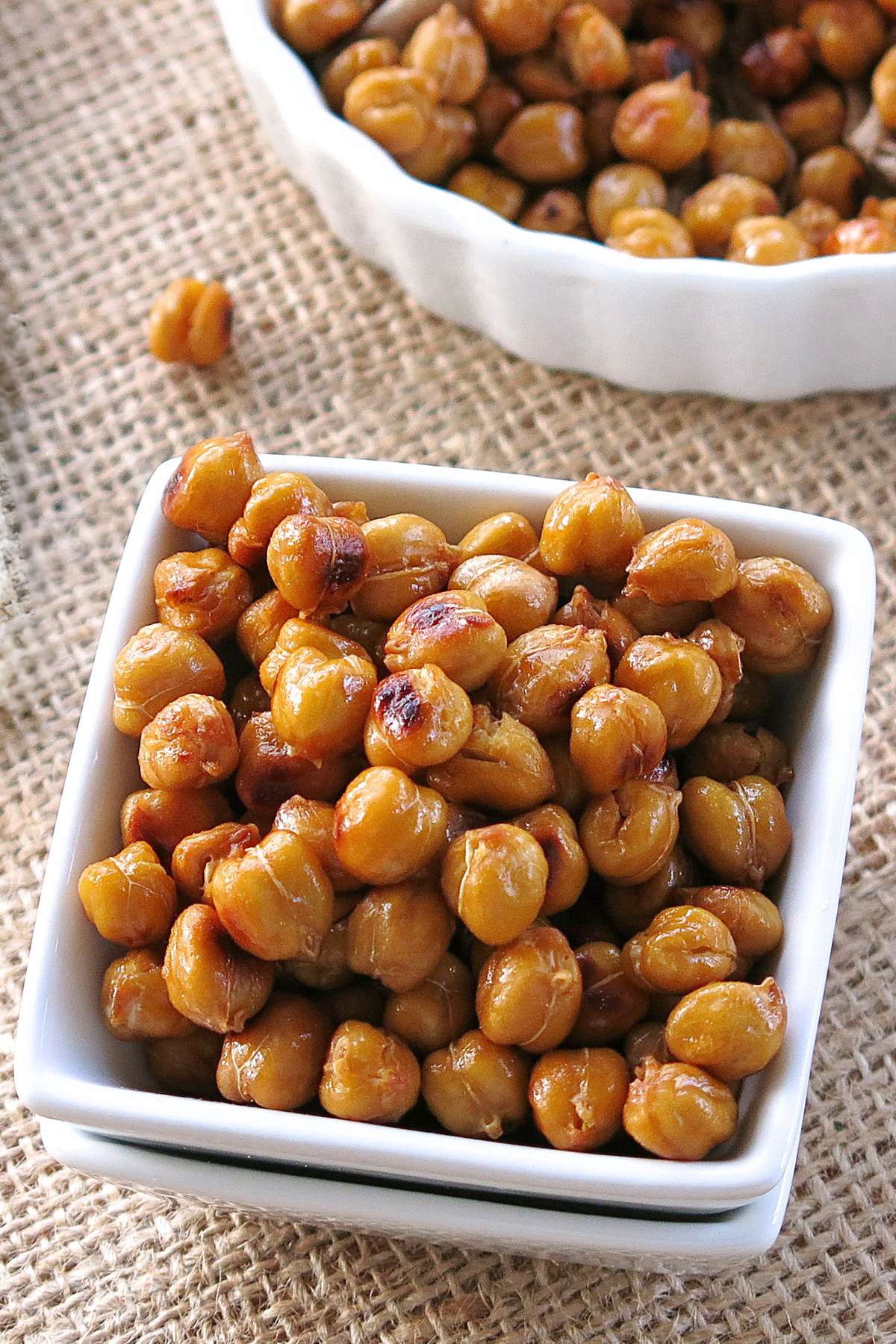 Roasted buffalo chickpeas in a stack of square white bowl with a bowl behind it with more chickpeas.