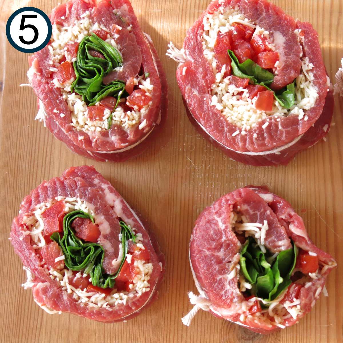 Four uncooked spinach stuffed steak pinwheels in a baking dish.