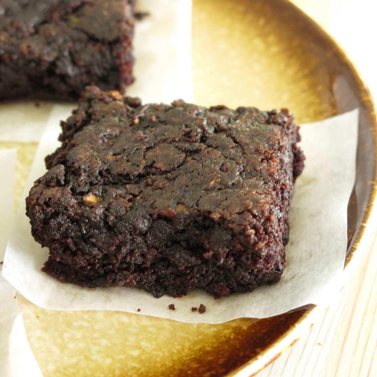 A single fudgy zucchini brownie on a plate with another partially shown behind it.
