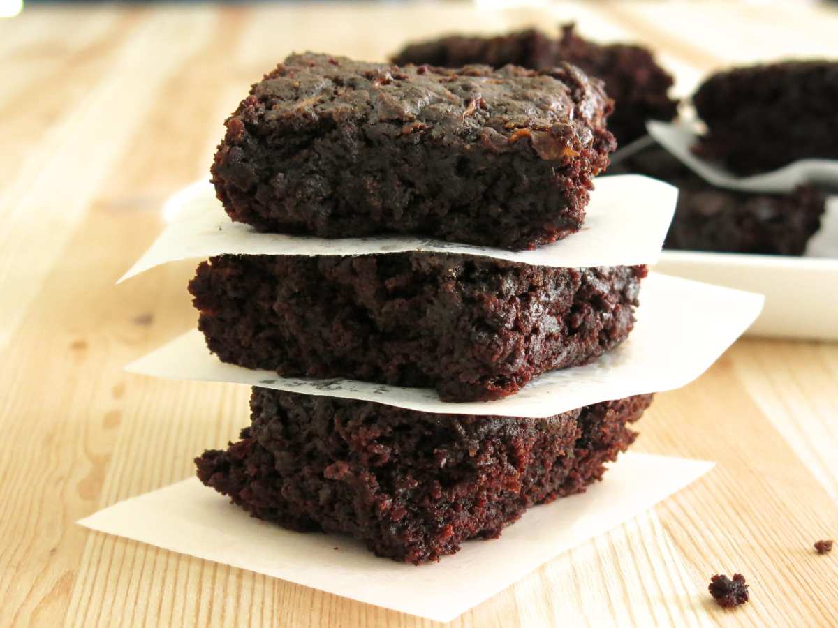Three zucchini brownies stacked on top of each other with parchment paper separating the pieces.