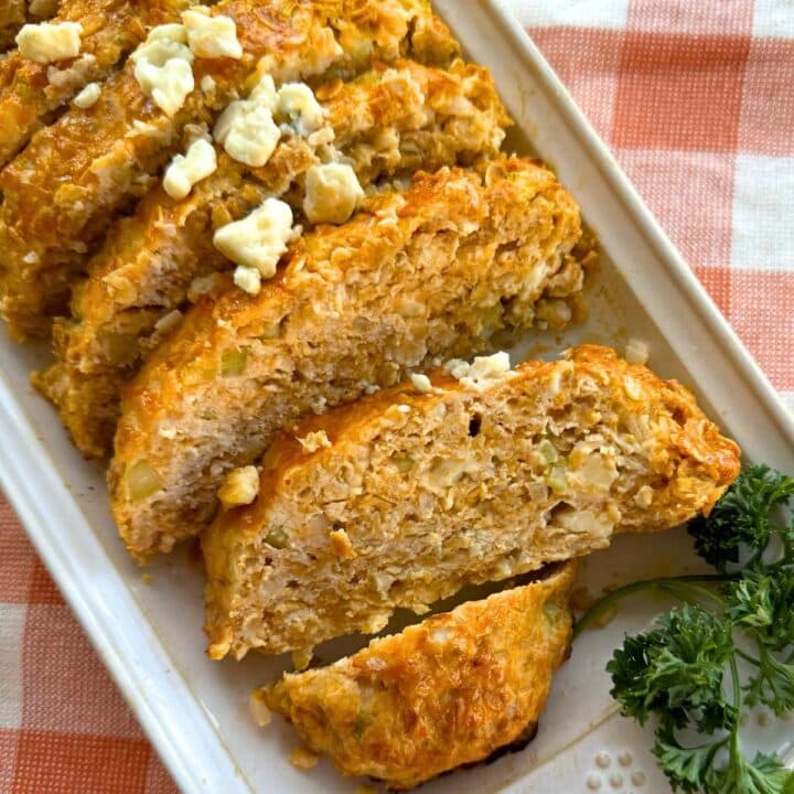 Buffalo chicken meatloaf sliced on platter and topped with crumbled blue cheese.