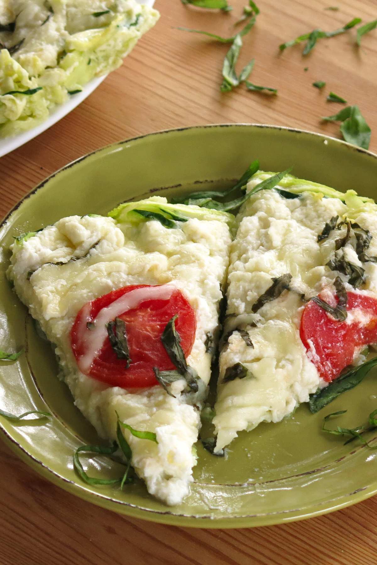 Two slices of crustless zucchini pie on a green plate with a plate with the crrust and chopped basil scattered behind it.