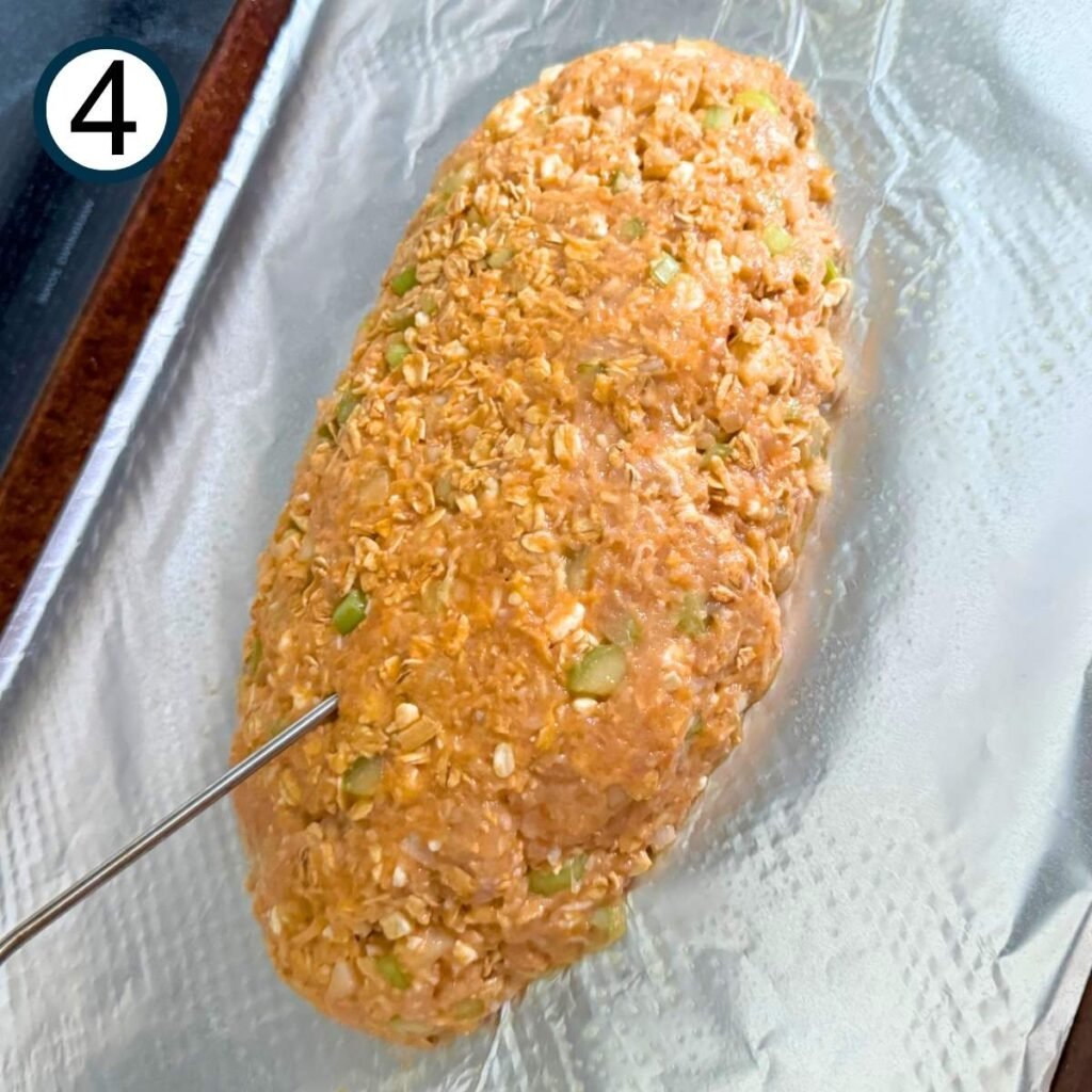 Buffalo chicken mixture formed into a meatloaf shape on a pan with a thermometer.