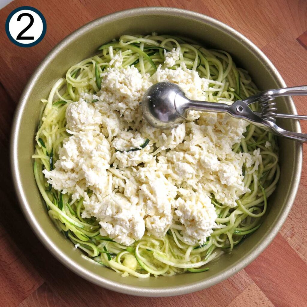 Spoon dropping mixture of mozzarella, ricotta, and Parmesan cheeses, on top of zucchini noodles.