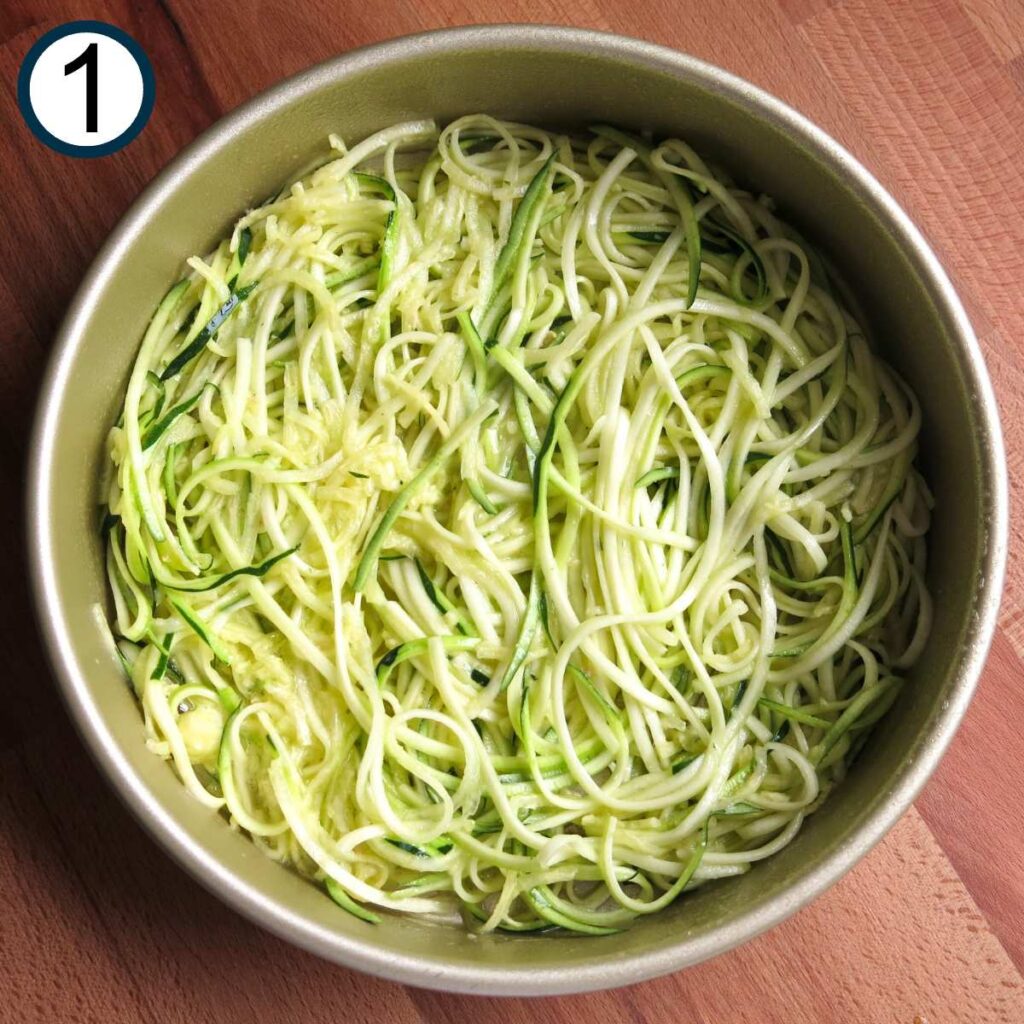 Spiralized zucchini noodles mixed with egg and olive oil in the bottom of a cake pan.