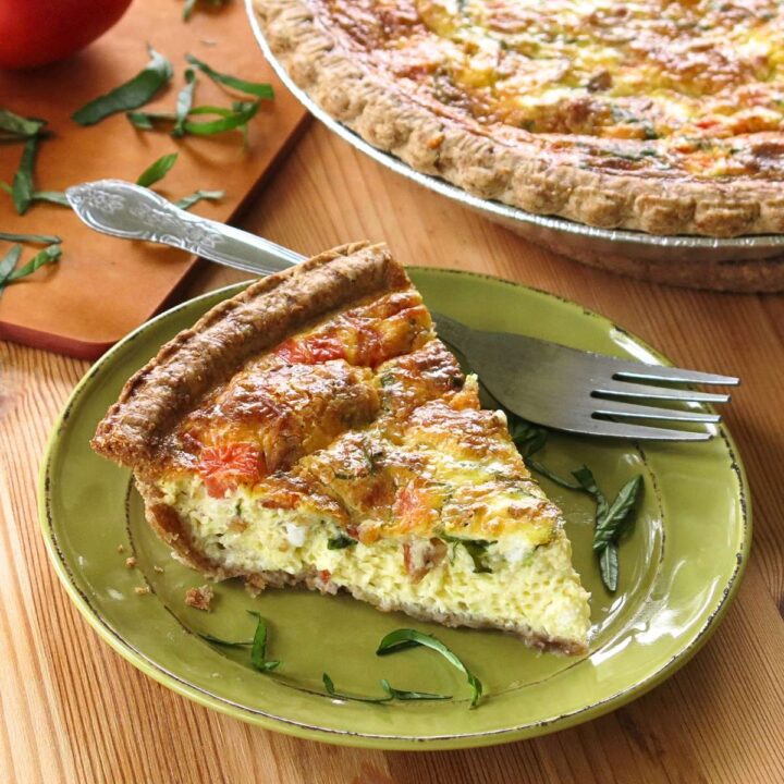 Slice of tomato bacon quiche on a green plate with a fork.