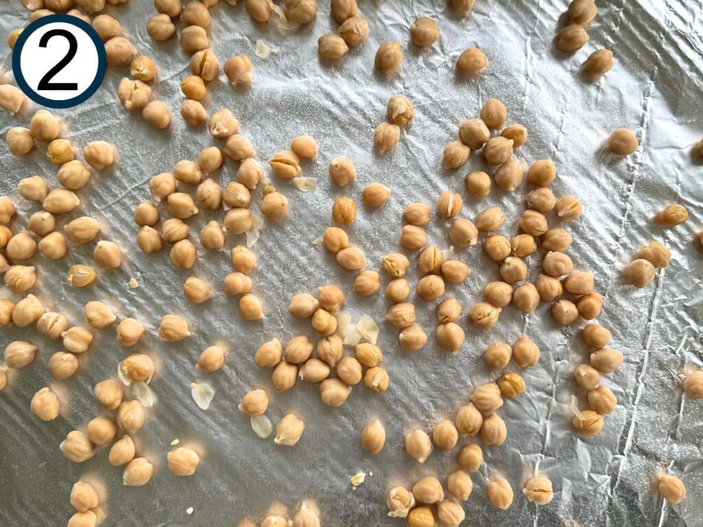 Uncooked chickpeas on a sheet pan lined with aluminum foil.