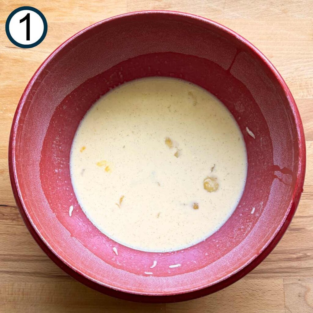 Whisked eggs, milk, salt, and white pepper in a red bowl.