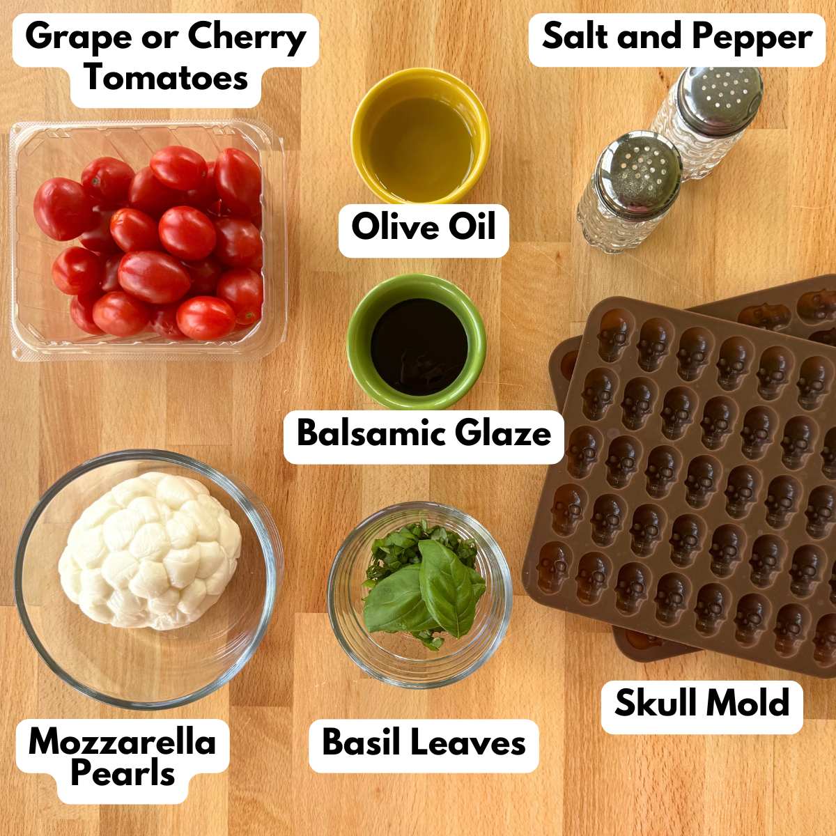 Ingredients to make Halloween caprese salad: grape tomatoes, mozzarella pears, balsamic glaze, olive oil, basil leaves, skull molds, salt, and pepper.