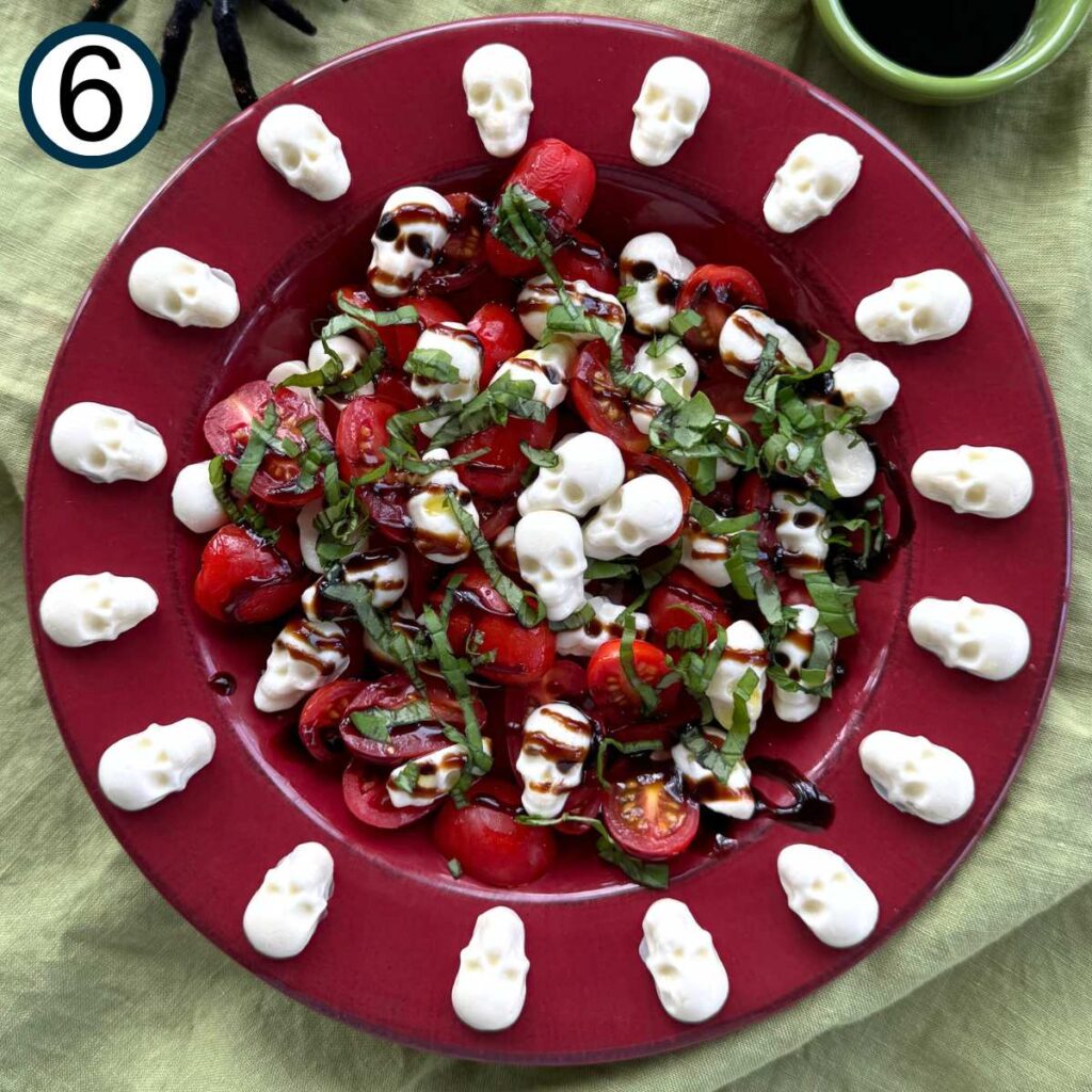 Red bowl with sliced tomatoes, skulls, topped with balsamic glaze and chopped fresh basil.