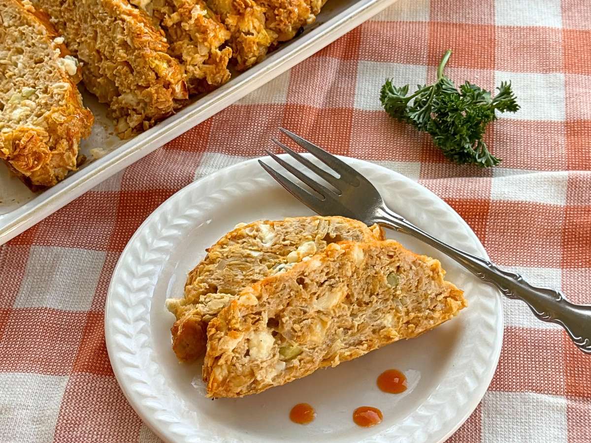Two slices of buffalo chicken meatloaf on a plate with dots of buffalo sauce.
