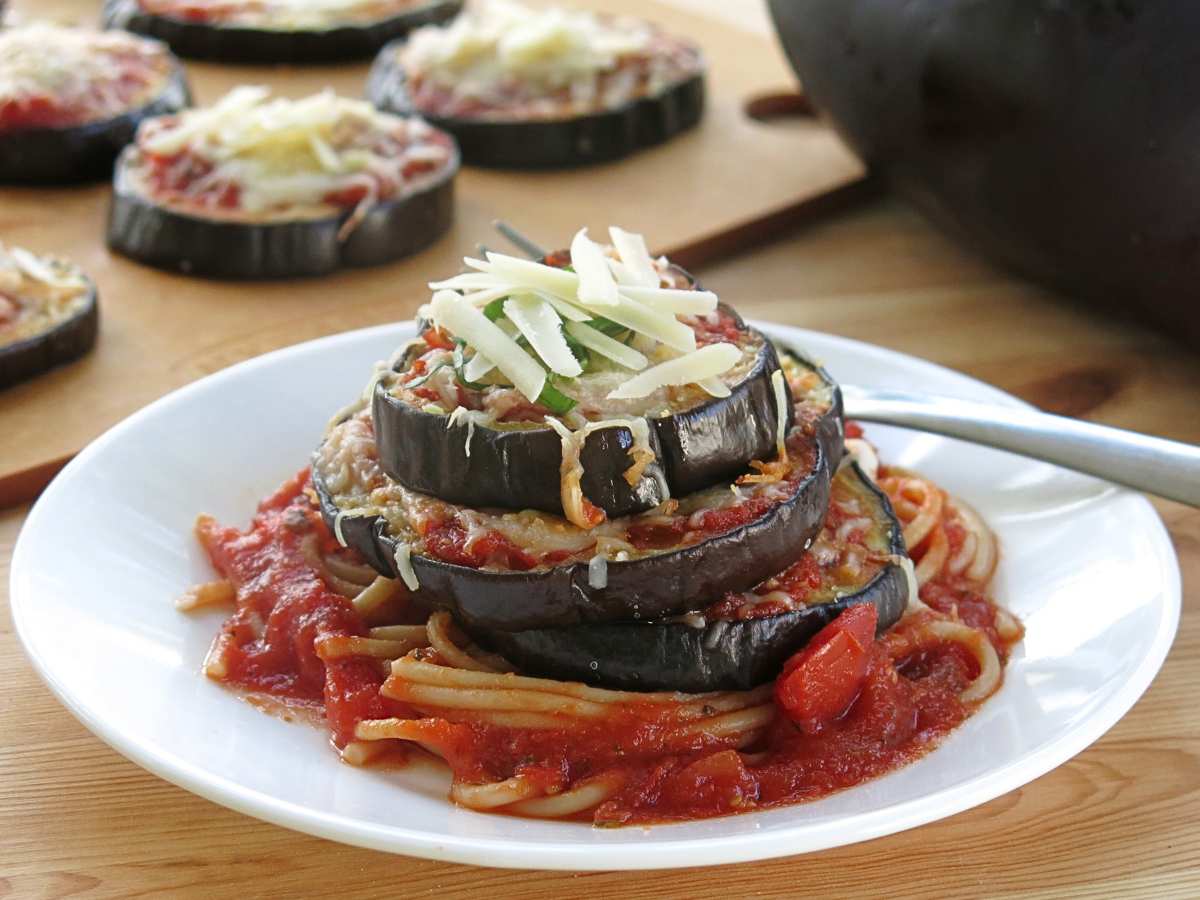 Unbreaded eggplant parmesan stacked three layers high on a white plate.