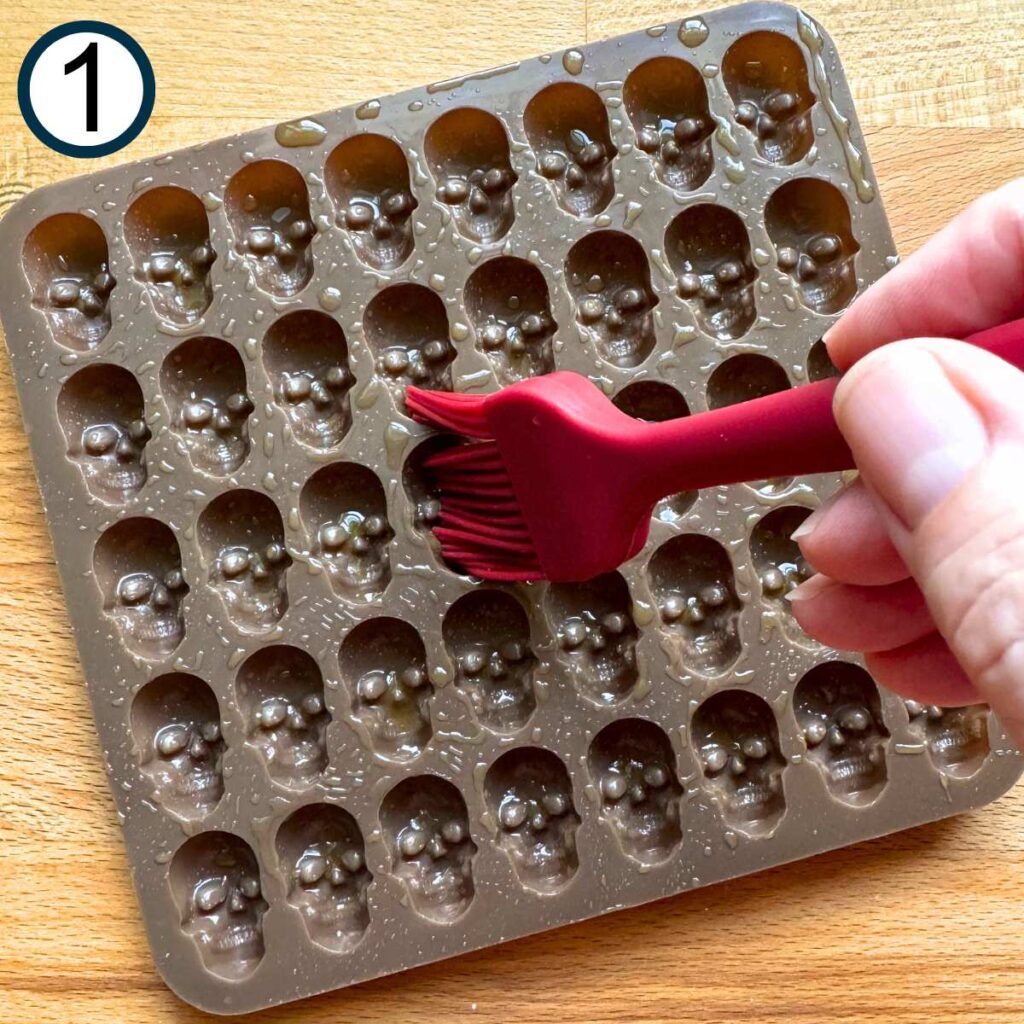 Hand brushing olive oil in skull candy mold.